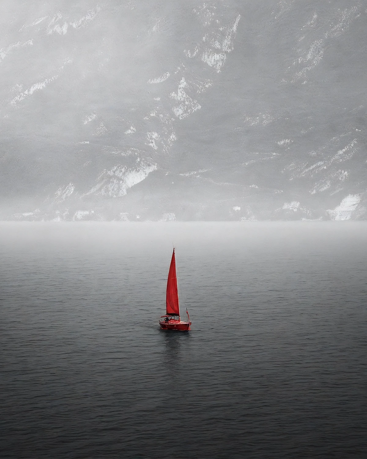 Small red sailboat inside a large silver seascape