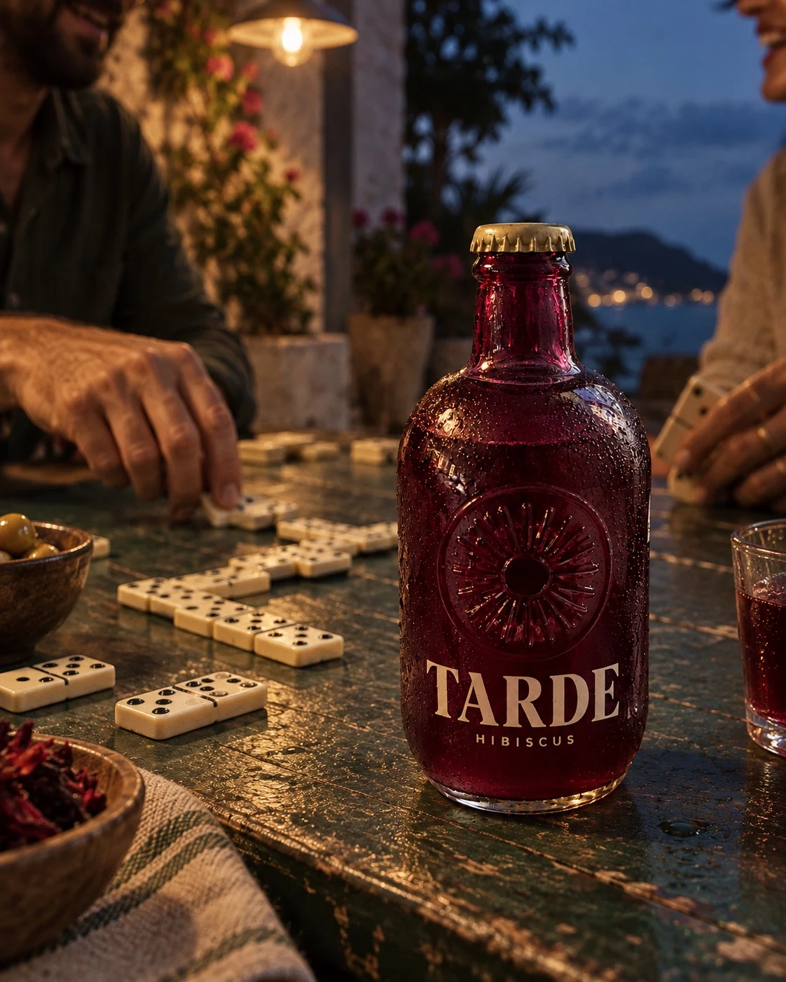 TARDE bottle beside friends playing dominoes at a green table at dusk