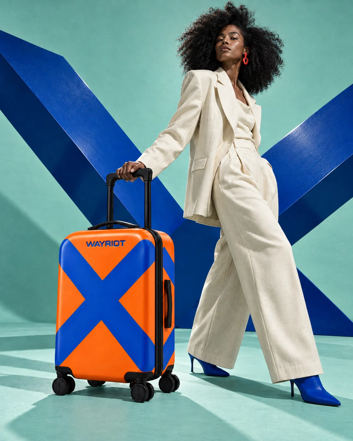 Model in ivory tailoring with the orange Bold X suitcase against mint and cobalt sculpture