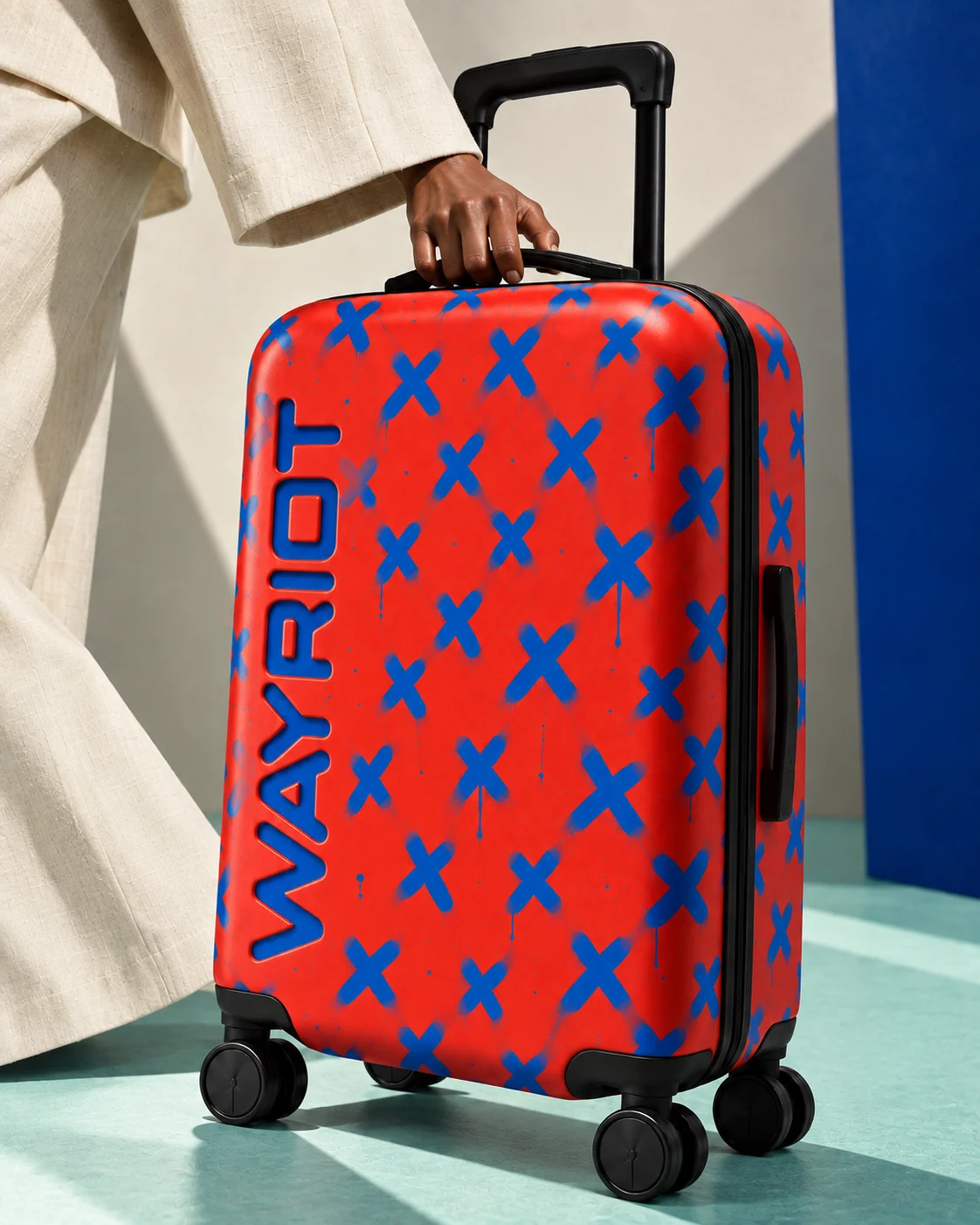 Red and cobalt Sprayed Xs suitcase held beside an ivory suit